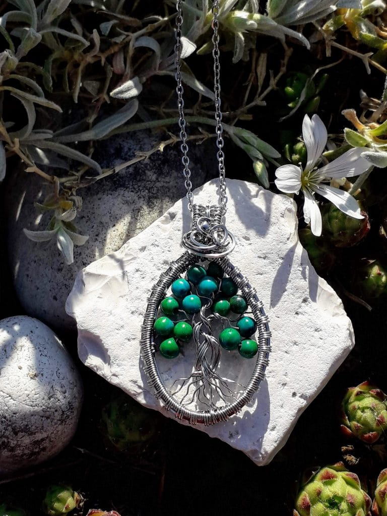 arbre de vie jade verte tissé fil acier inoxydable photographié sur une pierre blanche avec un fond nature et fleurs