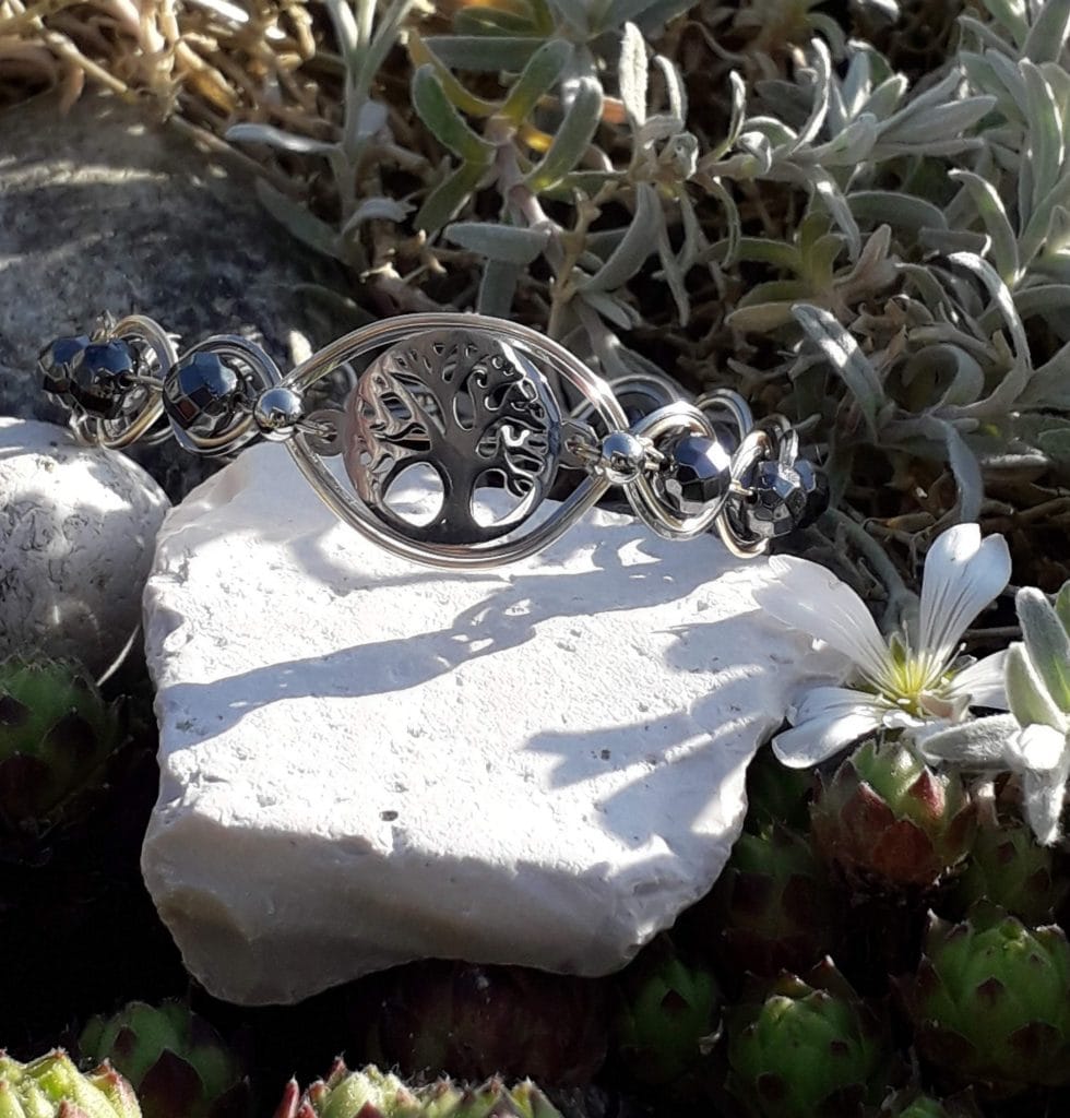 bracelet-arbre-de-vie-hematite-mcybijoux-nature photographie prise en extérieur sur une pierre blanche accompagnée d'une fleur