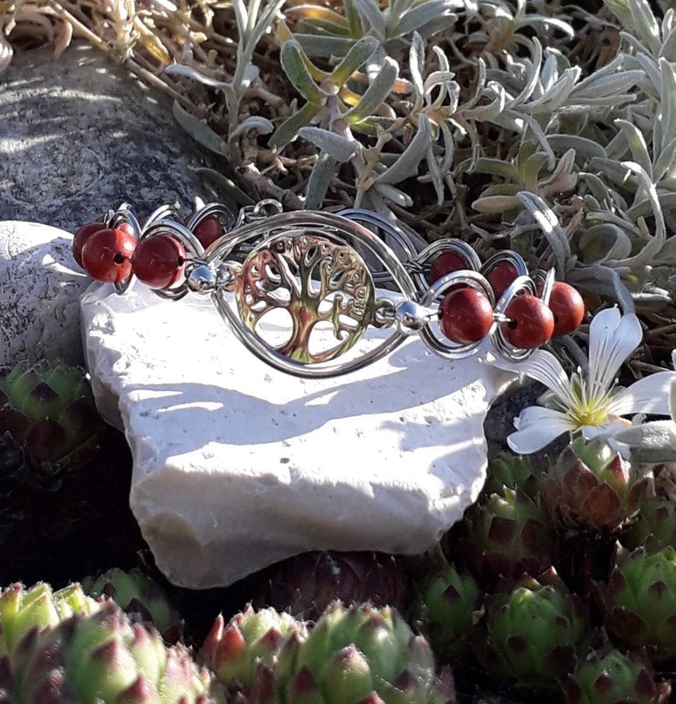 bracelet-arbre-de-vie-jaspe-rouge-mcybijoux-nature photographie prise en extérieur sur une pierre blanche accompagnée d'une fleur