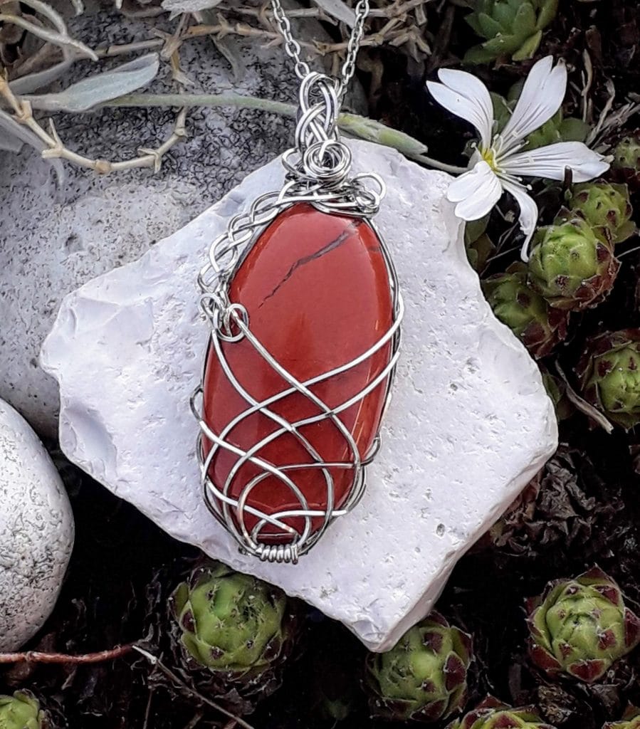 pendentif-jaspe-rouge-mcybijoux-nature photographié sur une pierre blanche avec une fleur en extérieur