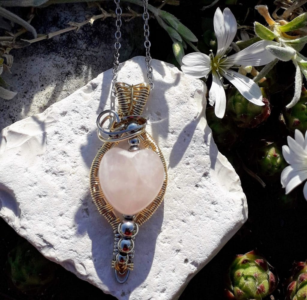 pendentif-quartz-rose-coeur-mcybijoux-nature photographie extérieure sur une pierre blanche et une fleur