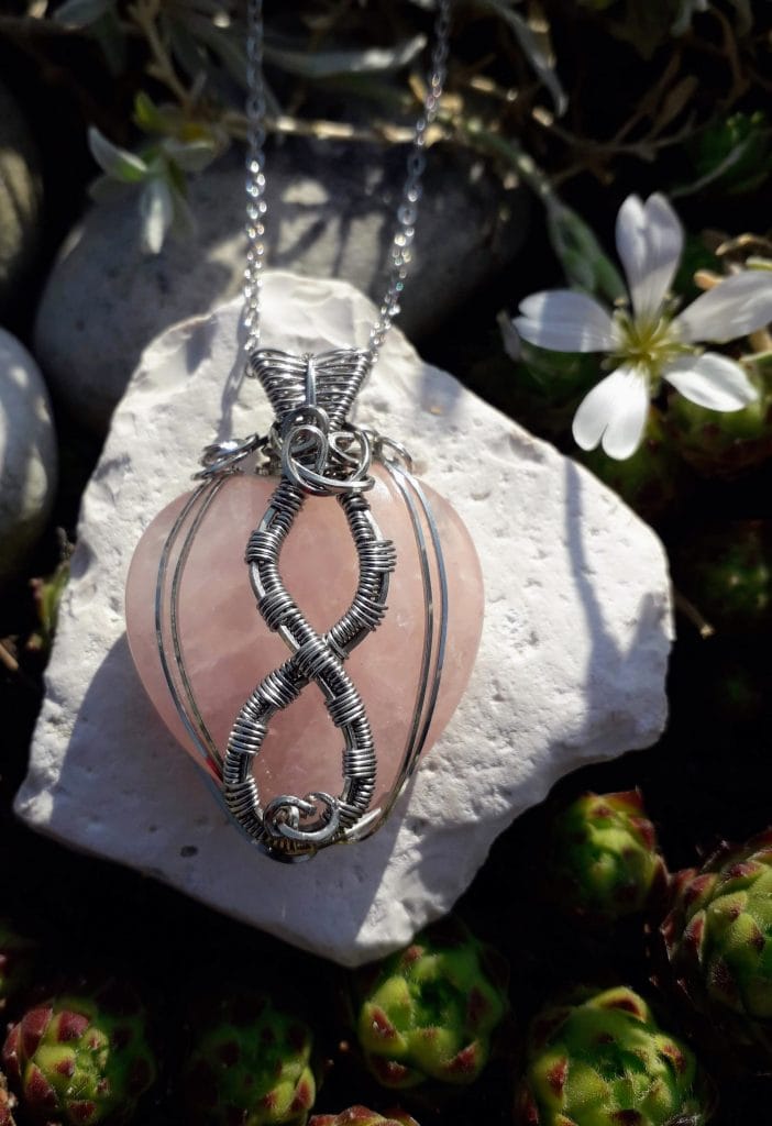pendentif-quartz-rose-symbole-infini-mcybijoux-nature photographie prise en extérieur sur une pierre blanche à côté d'une fleur