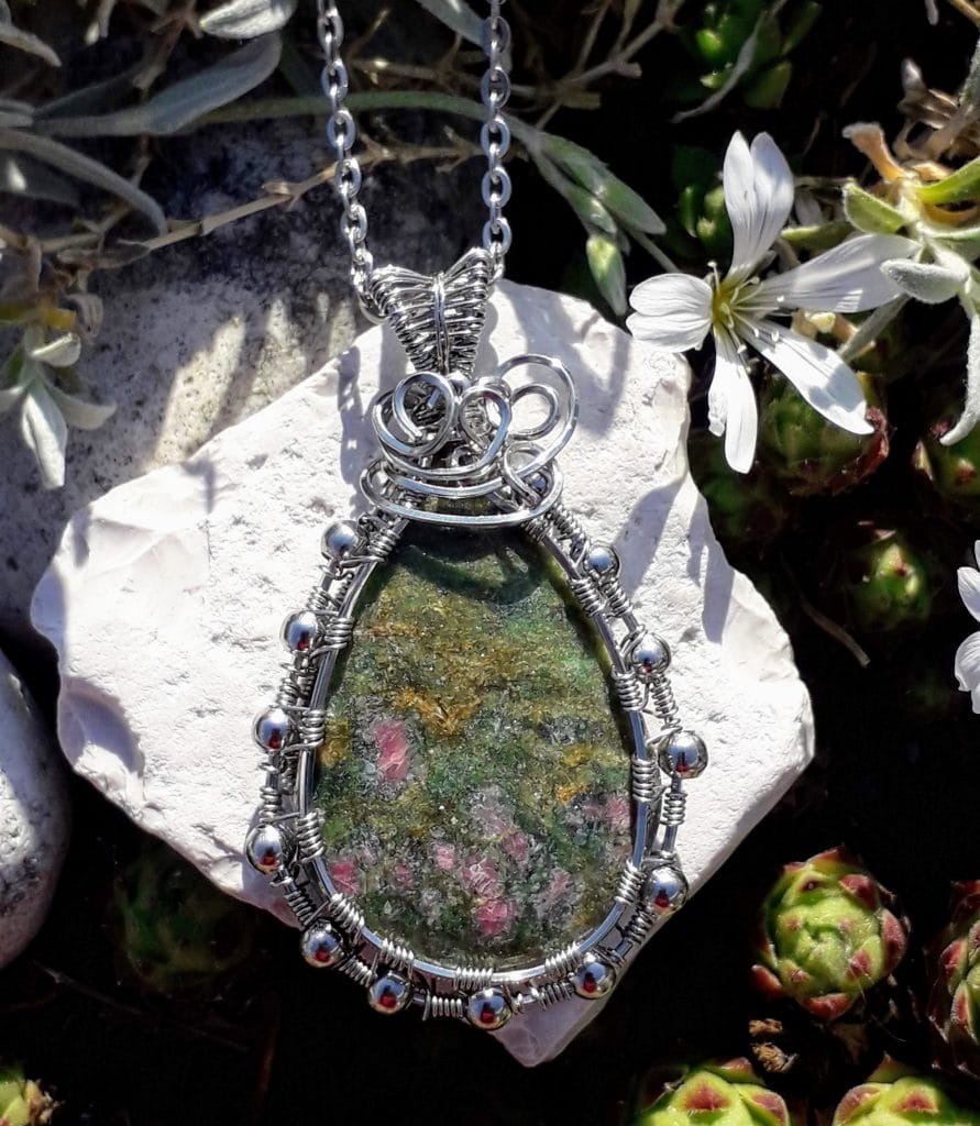 rubis-fuschite-pendentif-le-monde-en-cy-nature photographie prise en extérieur sur une pierre blanche avec une fleur