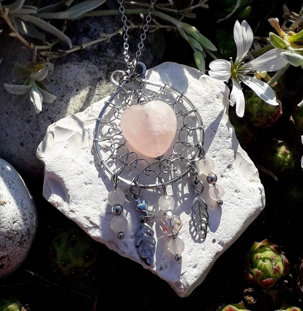 pendentif attrape-reves-quartz-rose-mcybijoux exposé sur une pierre blanche en extérieur à côté d'une fleur